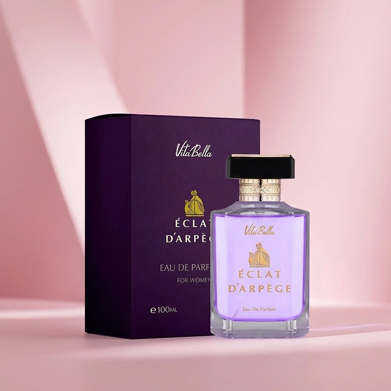 بطری بنفش ادکلن ویتابلا اکلت دی آرپژ در کنار جعبه تیره با طراحی لوکس و مینیمال روی پس‌زمینه صورتی ملایم