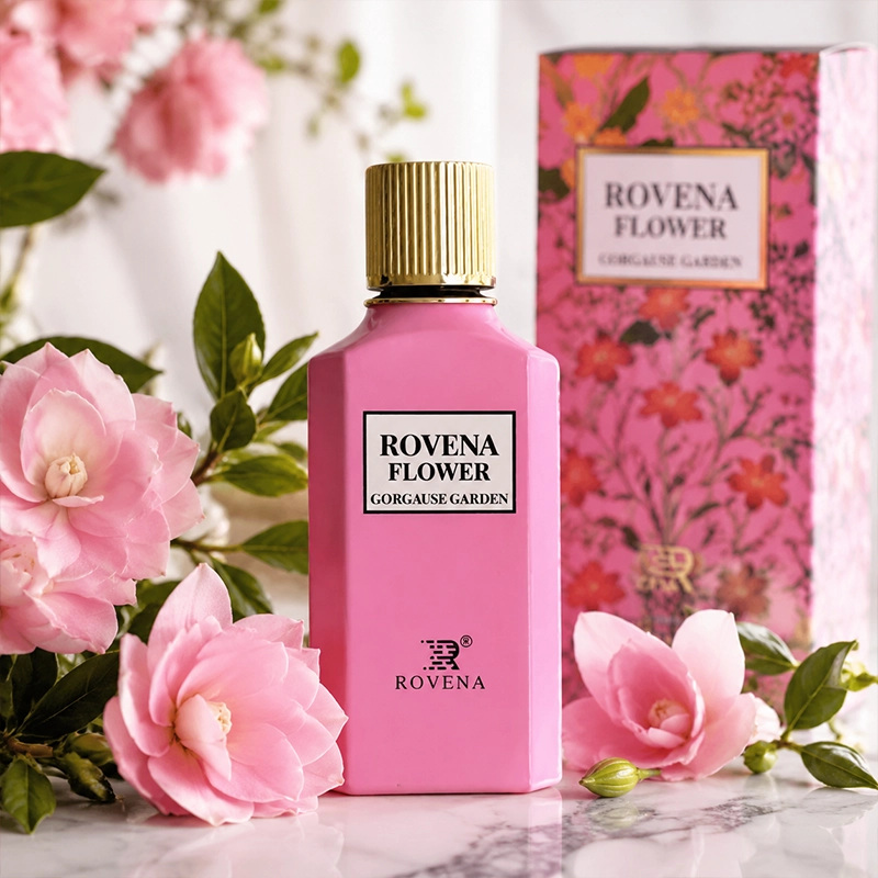 عطر ROVENA FLOWER صورتی با درب طلایی در میان گل‌های صورتی و سفید و شاخه‌های ظریف، با پس‌زمینه صورتی روشن